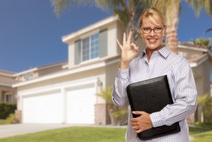 Attractive Businesswoman with Okay Hand Sign In Front of Nice Residential Home.